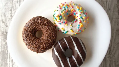 Three delicious sweet donuts rotating on a plate. Rustic wooden table. Looped Stock Footage 70807195