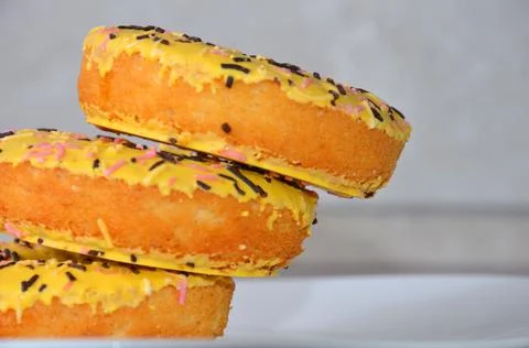 Three delicious yellow donuts with multi-colored sprinkles. Stock Photos