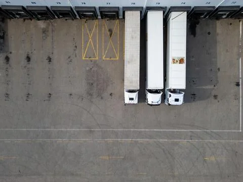 Three delivery trucks parked at loading docks of a warehouse, viewed from a.. Stock Photos