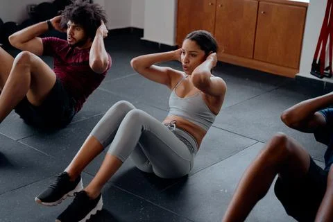 Three determined multiracial young adults doing sit-ups at the gym Stock Photos