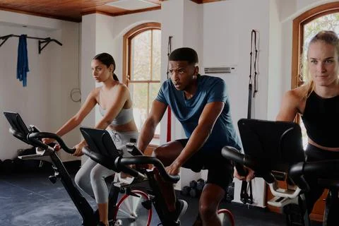 Three determined young multiracial adults doing cardio on exercise bike at the Stock Photos