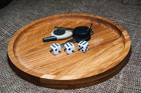 Three dice laying over a pile of money on a wooden plate Stock Photos