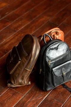 Three different colored leather backpacks on a wooden floor Stock Photos