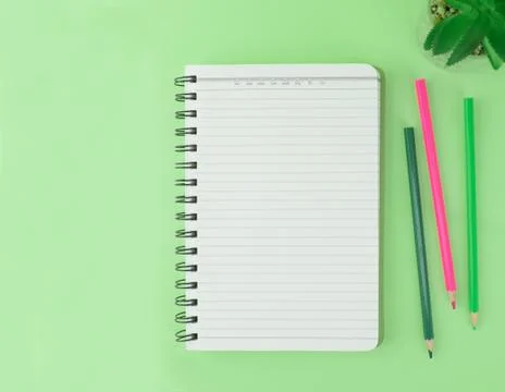 Three different colored pencil crayons scattered beside a notebook and a mini Stock Photos
