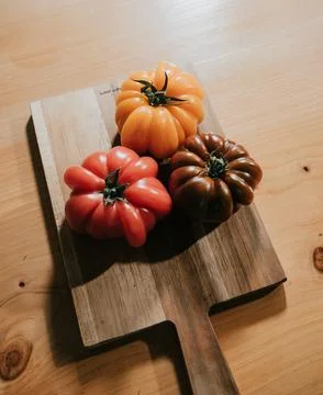 Three different colored tomatoes are on a wooden cutting board Stock Photos