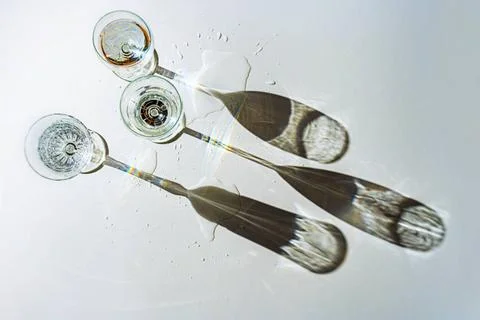 Three different drinking glasses filled with water are casting long shadow... Stock Photos