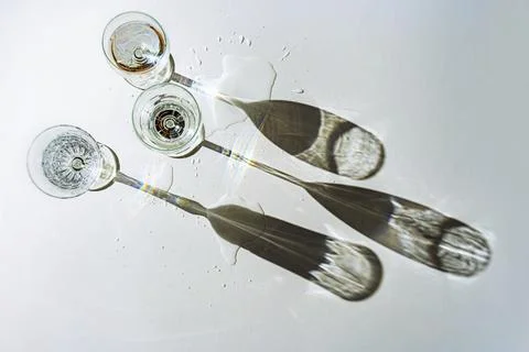Three different drinking glasses filled with water are casting long shadows on a Stock Photos