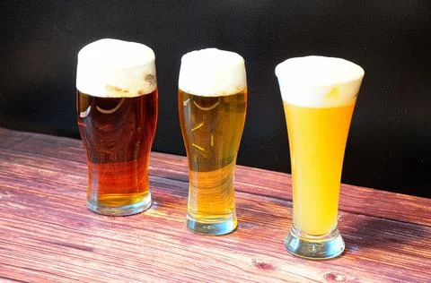 Three different glasses of light, wheat and dark beer with white foam stand i Foto stock