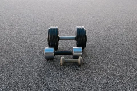Three different sized dumbbells lying on a textured grey surface, illustratin Stock Photos