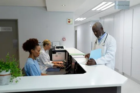 Three diverse male and female doctors in hospital reception using computers Stock Photos