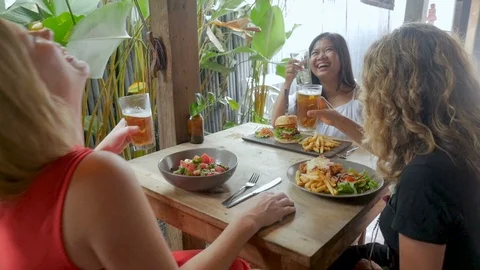 Three diverse women laughing and celebrating with drinks and lunch Stock Footage