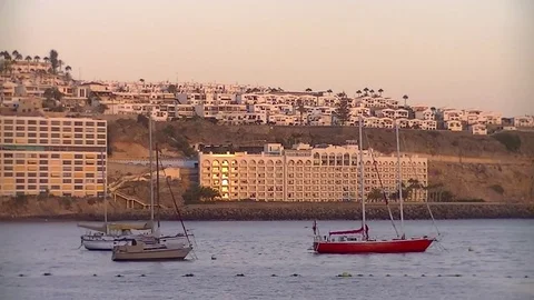 Three docked sailboats floating in the sea and coastline at dusk Stock Footage 80230742