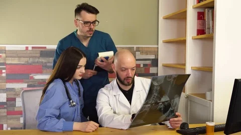 Three doctors are examining an X-ray at a table in the office in hospital Stock Footage 75683000