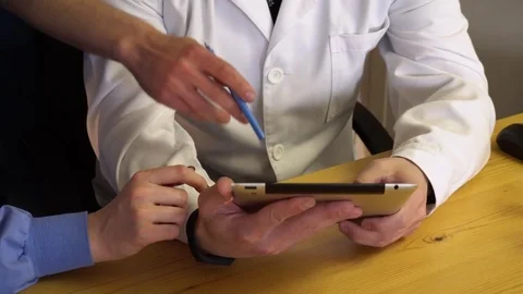 Three doctors are studying the results of the patient's tests on the tablet in Stock Footage 75682867