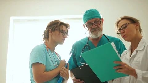 Three doctors conferring against the window in an emergency hospital, emergency Stock Footage 118853952