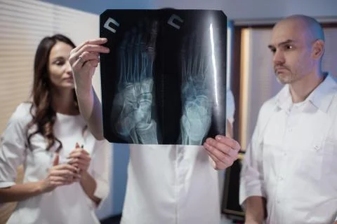 Three doctors look at an x-ray photo of a patient together Stock Photos