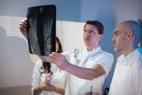 Three doctors look at an x-ray photo of a patient together Stock Photos