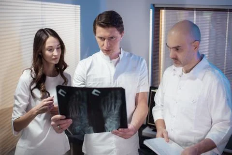 Three doctors look at an x-ray photo of a patient together Stock Photos