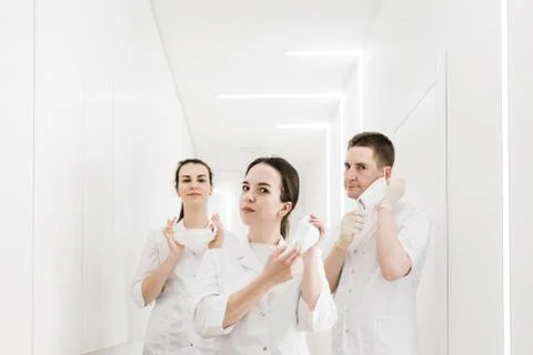 Three doctors remove protective medical masks in the white modern corridor of Stock Photos