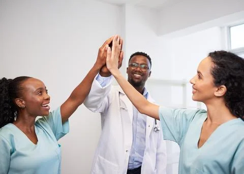 Three doctors share a high five, smile in hospital celebrate success Stock Photos