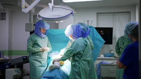 Three doctors wearing protective suits and helmets stand over the patient. Stock Footage 241124571