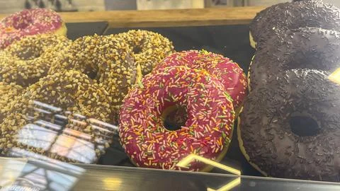 Three donuts with different toppings are displayed in a glass case Stock Photos