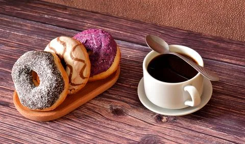 Three donuts in multi-colored glaze and a cup of hot black coffee on a sauc.. Stock Photos