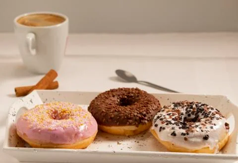 Three donuts on a white tray with a cup of coffee Stock Photos