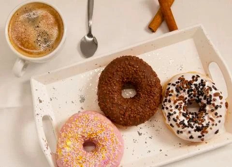 Three donuts on a white tray with a cup of coffee Stock Photos