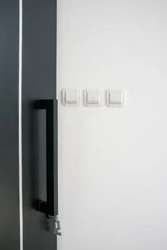 Three double and single light switch on white wall with black door in foreg.. Stock Photos