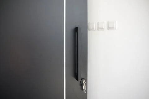 Three double and single light switch on white wall with black door in foreg.. Stock Photos