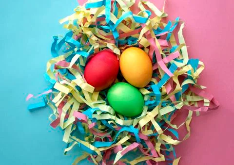 Three dyed Easter eggs in a colorful nest on mixed pink and blue background Stock Photos
