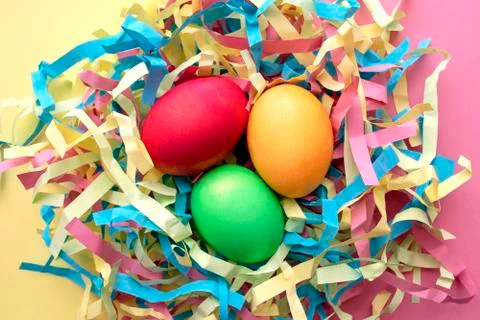 Three dyed Easter eggs in a colorful nest on mixed pink and yellow background Stock Photos