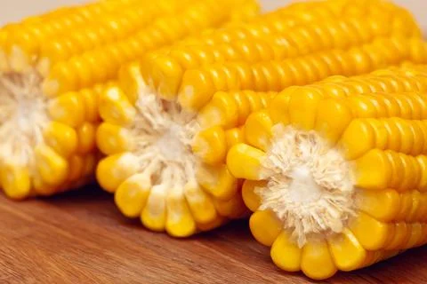 Three ears of boiled hot corn on a wooden board close-up. Stock Photos