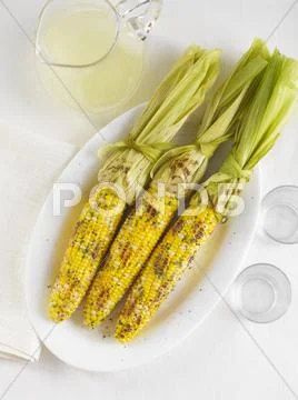 Three Ears of Grilled Corn on the Cob with a Pitcher of Lemonade Stock Photos