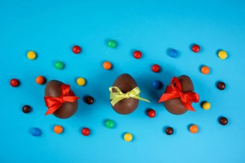Three Easter chocolate eggs among colorful dragee on the blue background. Stock Photos