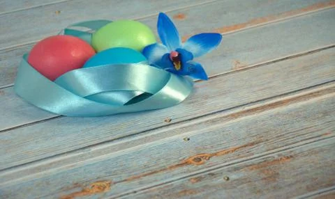 Three Easter eggs with a blue satin ribbon and an orchid bud on a wooden tabl Stock Photos
