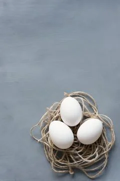 Three Easter eggs decorated with twine in the shape of a nest on a gray textu Stock Photos