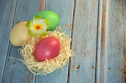 Three Easter eggs with decorative balls and a flower lie on the straw on a wo Stock Photos
