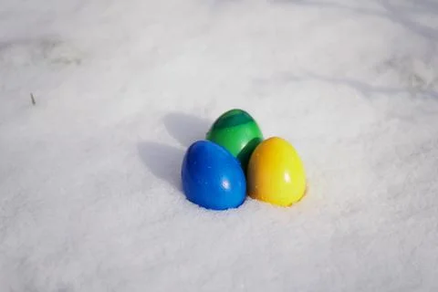 Three easter eggs painted in vibrant colors in fresh snow Stock Photos