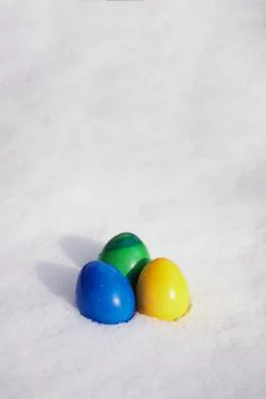 Three easter eggs painted in vibrant colors in fresh snow Stock Photos