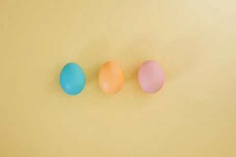 Three Easter eggs in pink, yellow and blue colors on a yellow background Stock Photos