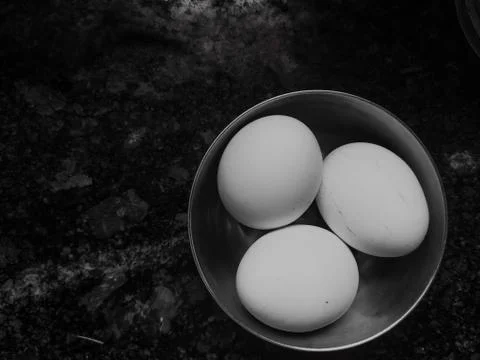 Three easter eggs in single bowl on marble tiled floor. Black background. Stock Photos