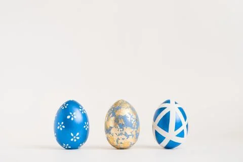 Three Easter golden decorated eggs on blue background. Minimal easter concept Stock Photos