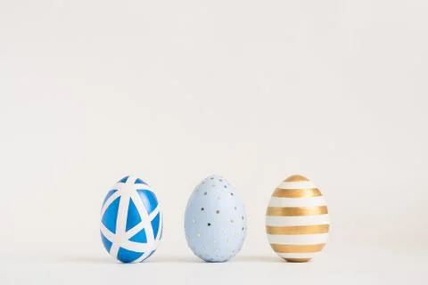 Three Easter golden decorated eggs on blue background. Minimal easter concept Stock Photos
