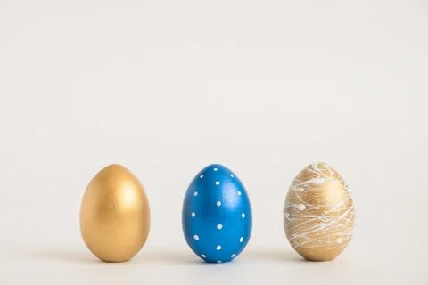 Three Easter golden decorated eggs on blue background. Minimal easter concept Stock Photos