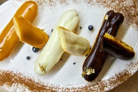 Three eclair cakes in caramel, cream and chocolate glaze on a white plate Stock Photos