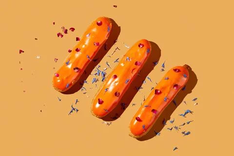 Three eclairs with orange glaze and custard on an orange background. Creati.. Stock Photos