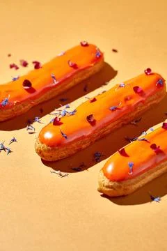 Three eclairs with orange glaze and custard on an orange background. Creati.. Stock Photos