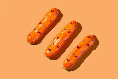 Three eclairs with orange glaze and custard on an orange background. Creati.. Stock Photos